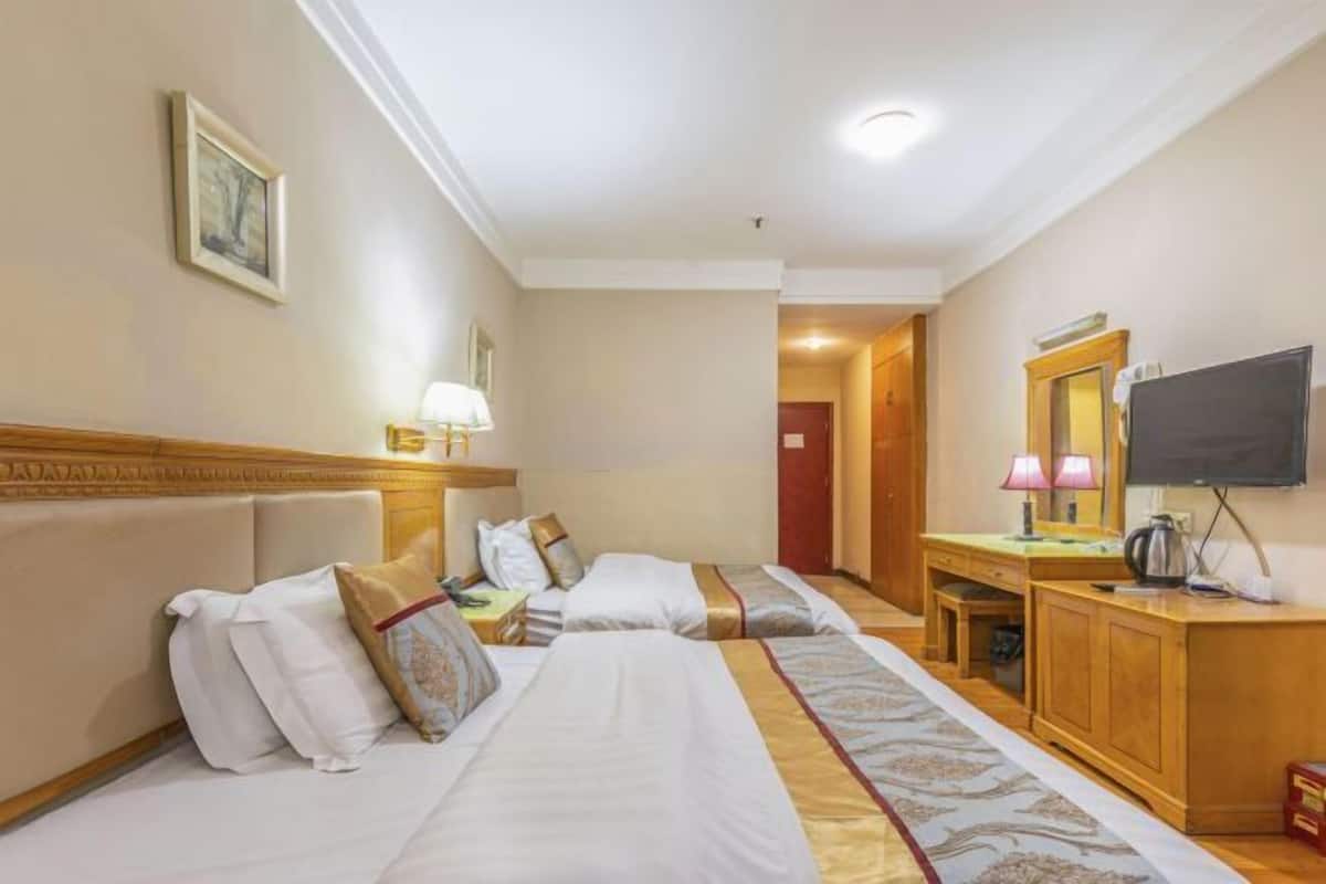 A hotel room with two beds, a desk, a television, and a mirror.
