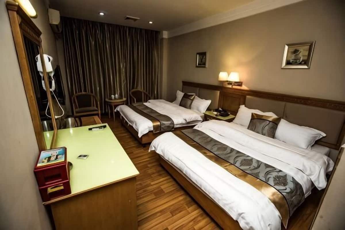 A hotel room with two beds, a desk, a chair, a lamp, and a picture on the wall.