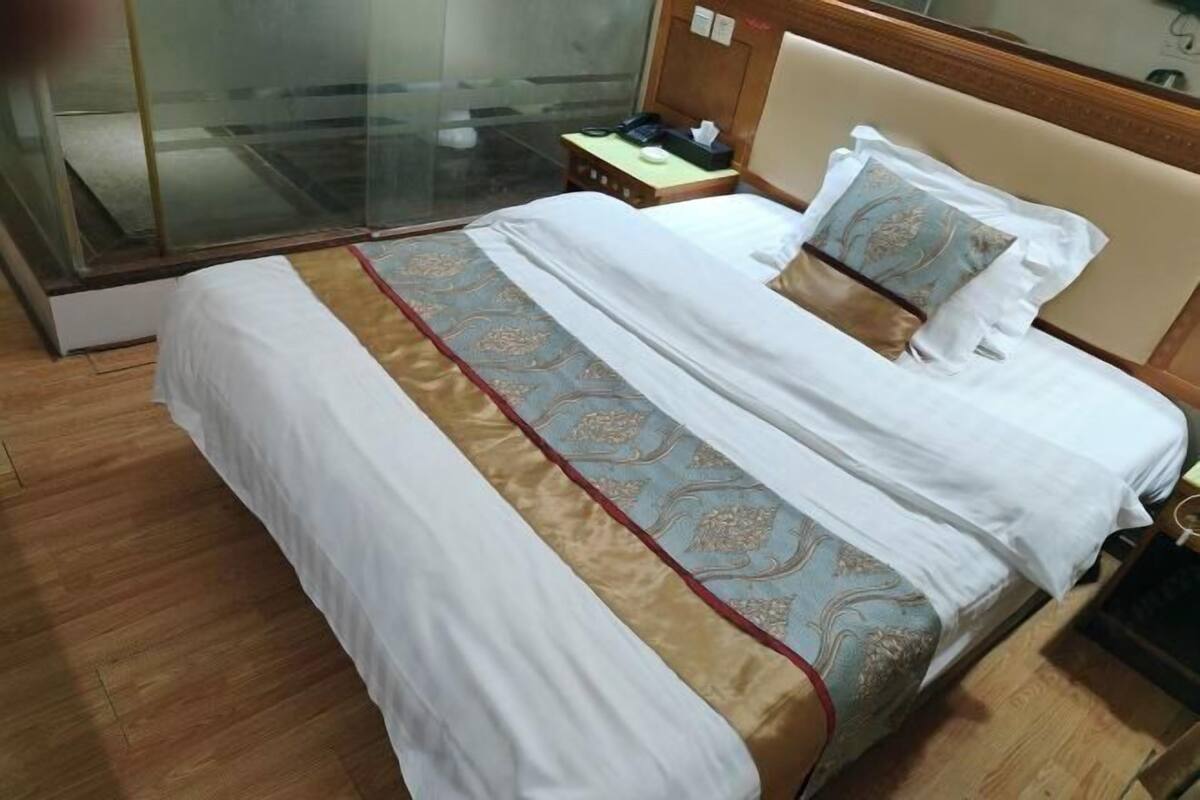 A hotel room with a bed, a bedside table, a nightstand, and a glass partition.