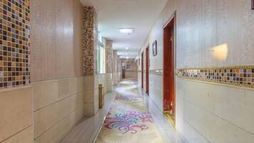 A hotel corridor with patterned walls, a decorative carpet, and doors leading to rooms.
