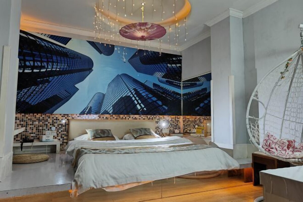 A modern bedroom with a large bed, a hanging chair, and a cityscape mural on the wall.