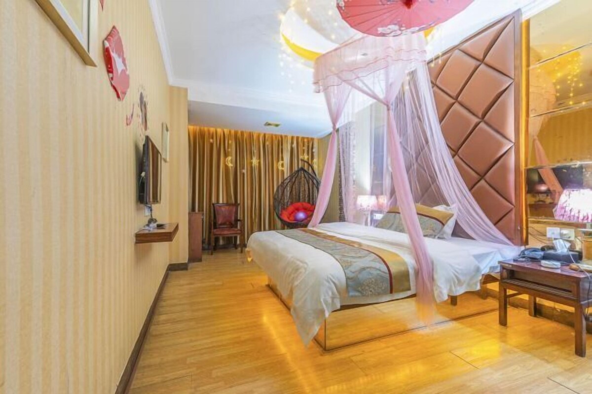 A bedroom with a canopy bed, a television, a chair, and a bedside table.