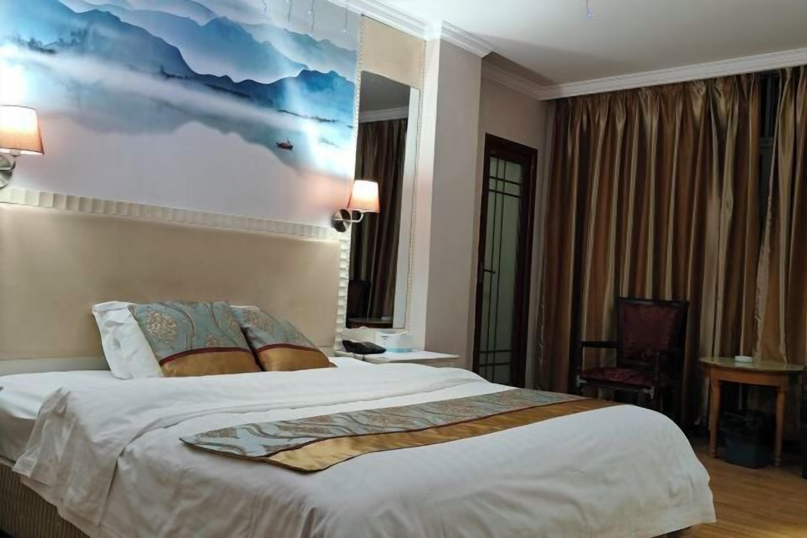 Una habitación de hotel con una cama, una silla, una mesita, un cuadro en la pared y cortinas.