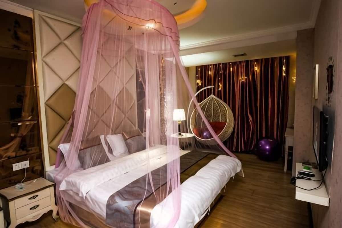 A bedroom with a canopy bed, a bedside table, a lamp, a decorative chair, and a television.