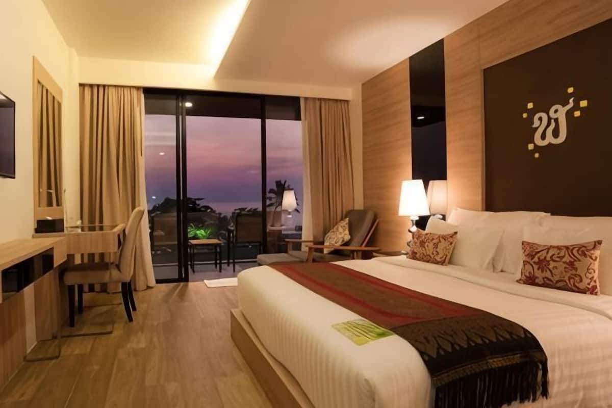 A hotel room with a large bed, a desk, a chair, a TV, and a view of the outside.