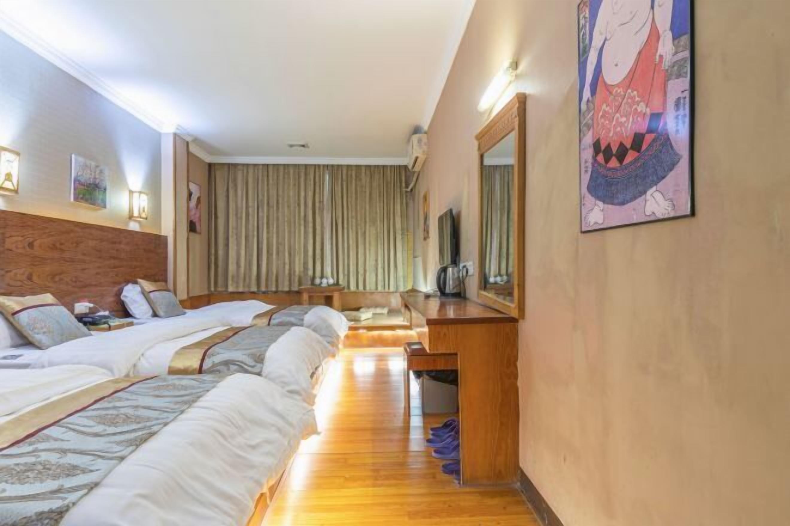 Une chambre d’hôtel avec deux lits, un bureau en bois, un miroir et une œuvre d’art accrochée au mur.