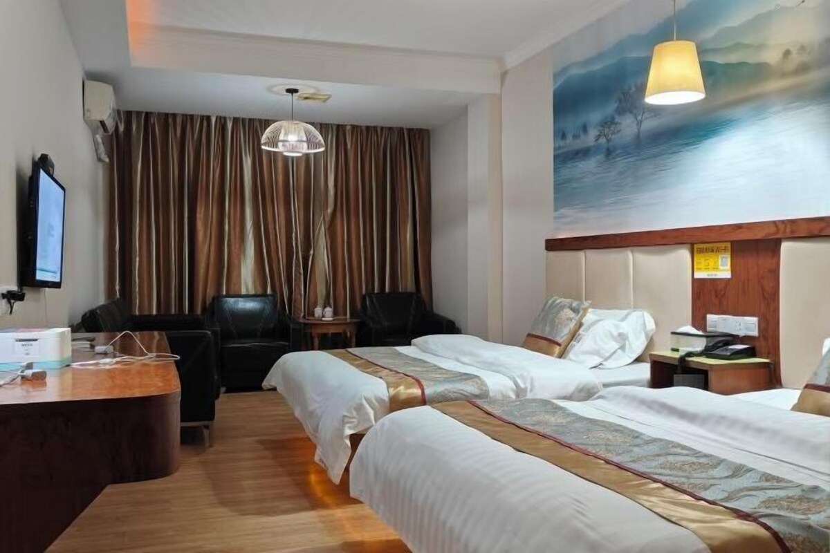 A hotel room with two beds, a desk, a chair, a painting on the wall, and a ceiling light.