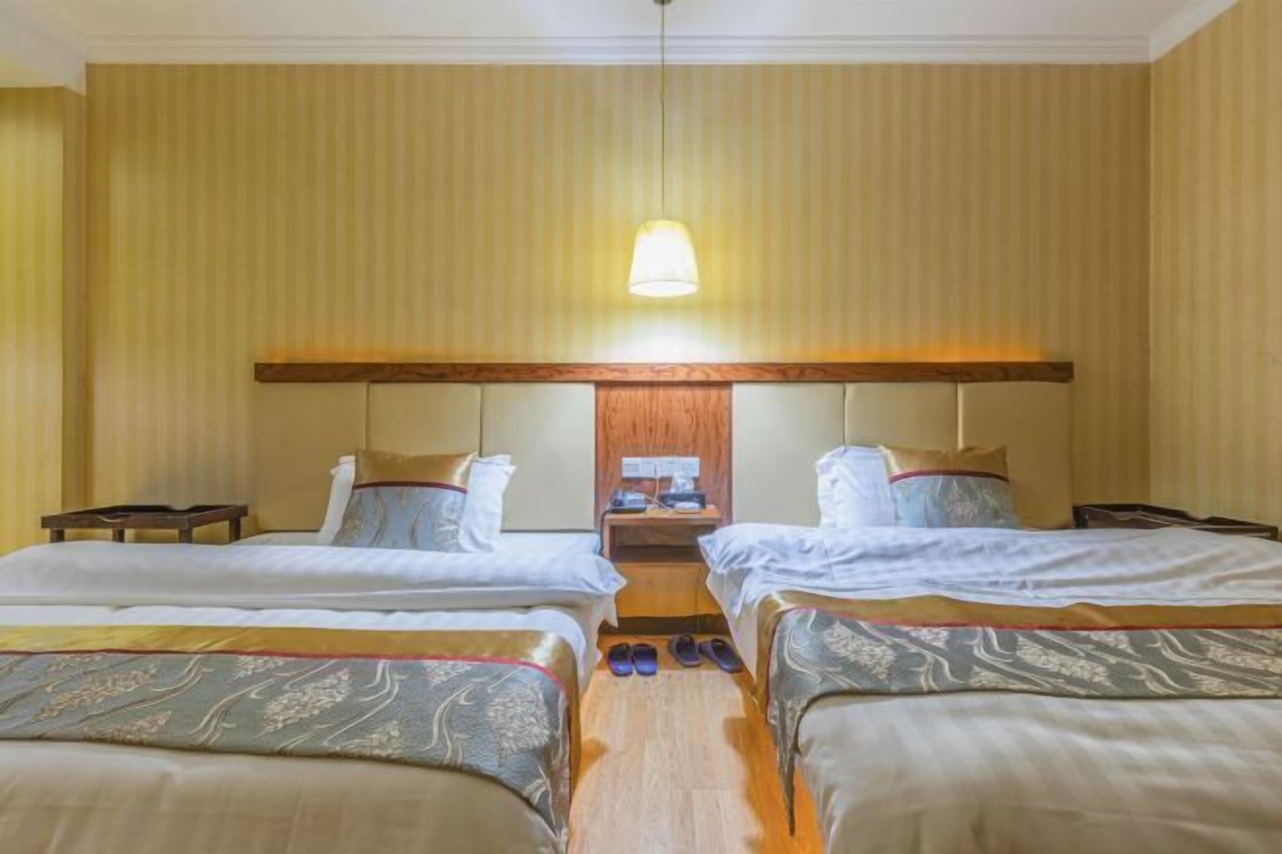 A hotel room with two beds, a wooden headboard, a nightstand, and a hanging lamp.