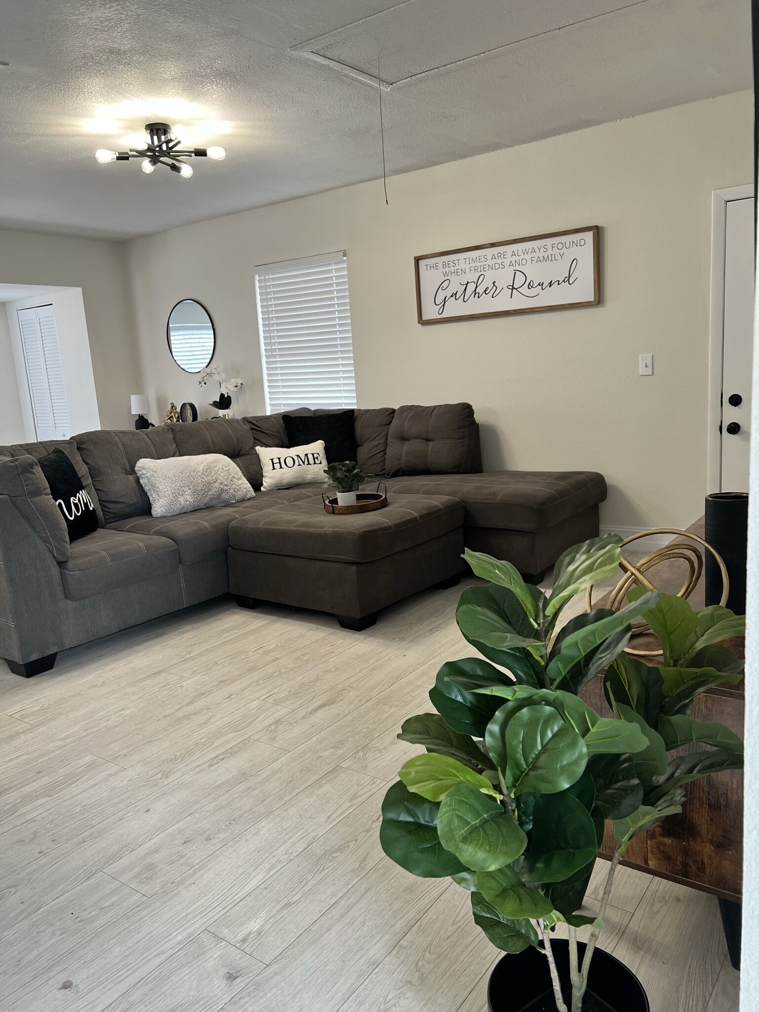 A modern living room with a sectional sofa, a ceiling fan, and a motivational quote on the wall.