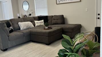 A modern living room with a sectional sofa, a ceiling fan, and a motivational quote on the wall.