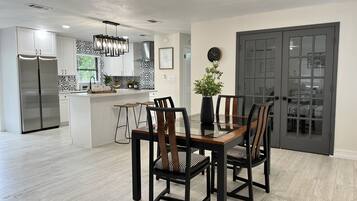 A modern kitchen with a central island, stainless steel appliances, and a dining area with a glass table and wooden chairs.