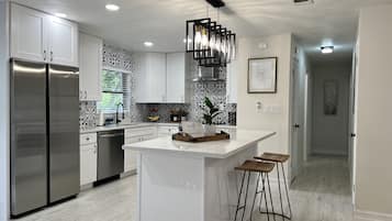 A modern kitchen with white cabinetry, a stainless steel refrigerator, a central island with stools, and a patterned backsplash.
