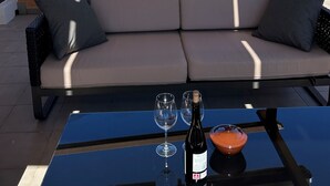 Un balcón con un sofá y una mesa, una botella de vino y dos copas sobre la mesa.