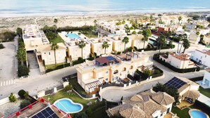 Un resort costero con varias construcciones, piscina y palmeras.