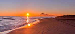 Una playa con un atardecer, olas y una montaña al fondo.