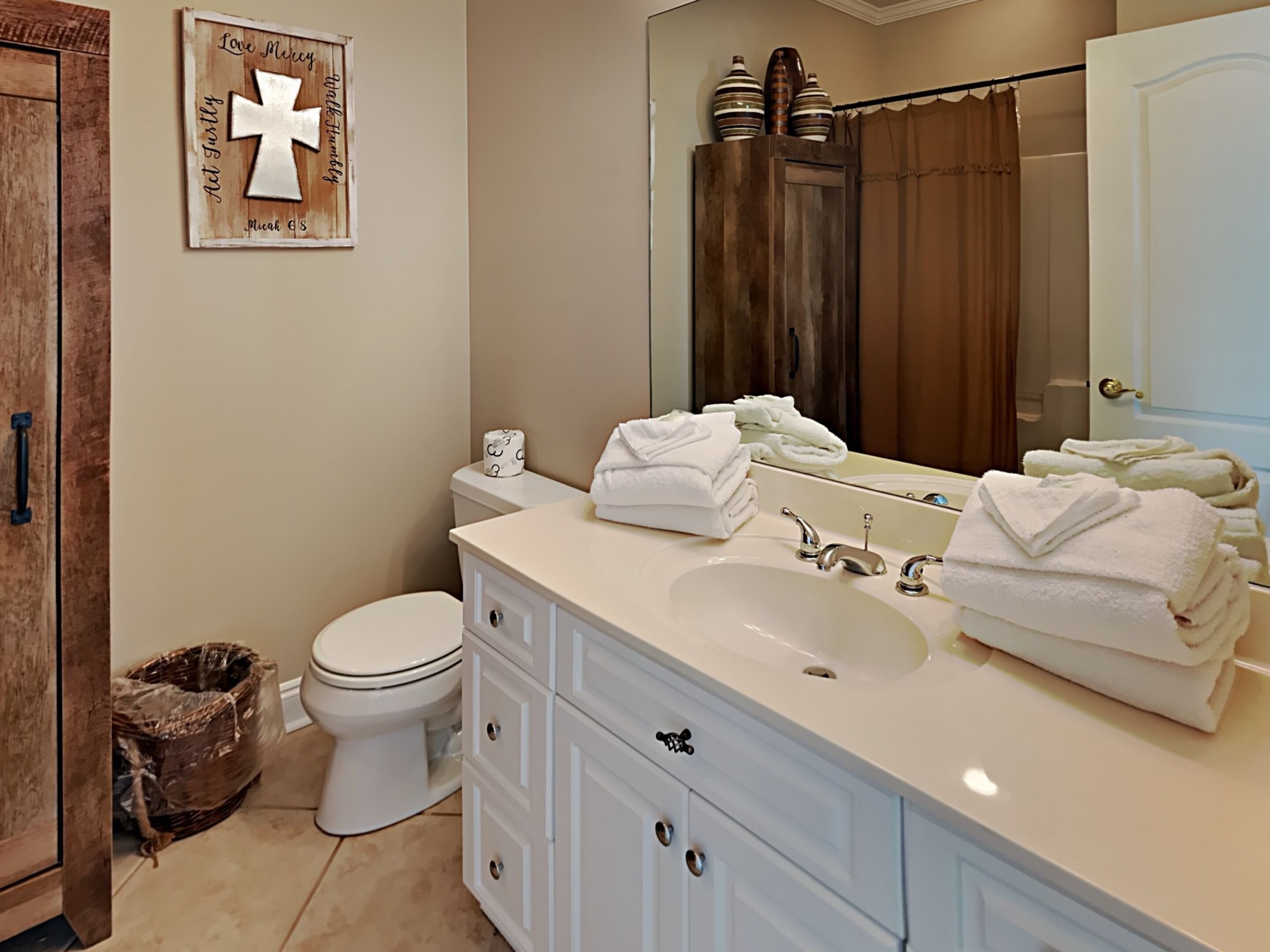 Une salle de bain avec un lavabo blanc, deux piles de serviettes, des toilettes et un meuble en bois.