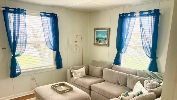 Una sala de estar con un sofá seccional color beige, un pequeño reposapiés y un cuadro en la pared.