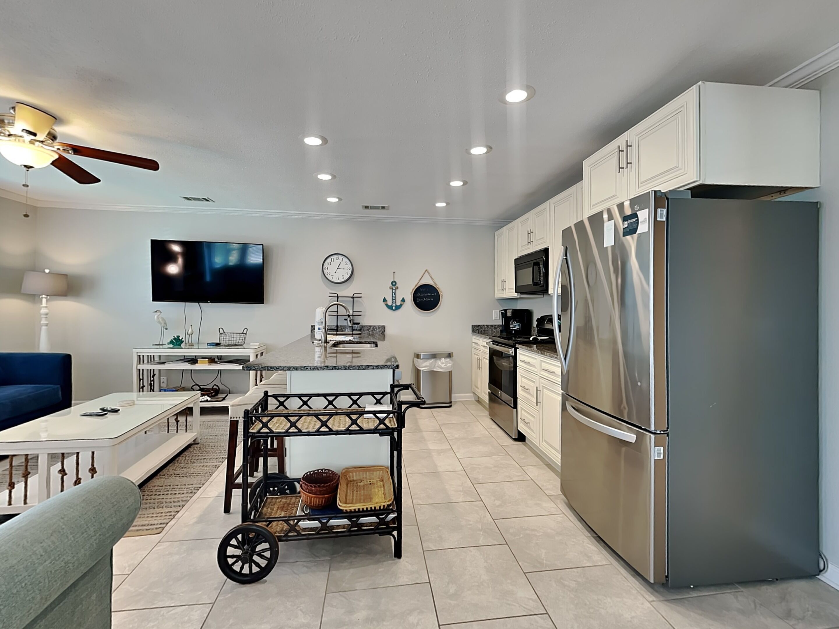 Una cocina moderna con armarios blancos, un refrigerador de acero inoxidable y una zona de comedor con una mesa blanca y un sofá azul.