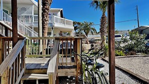 A wooden deck with a bicycle leaning against a post, surrounded by gravel and palm trees.