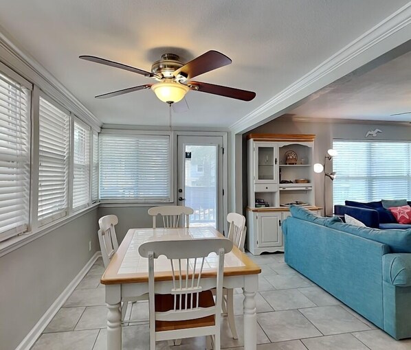 A dining area with a table and chairs, a ceiling fan, and a blue sofa in the adjacent living room. - Sangria Dreams by Southern Vacation Rentals (Miramar Beach)
