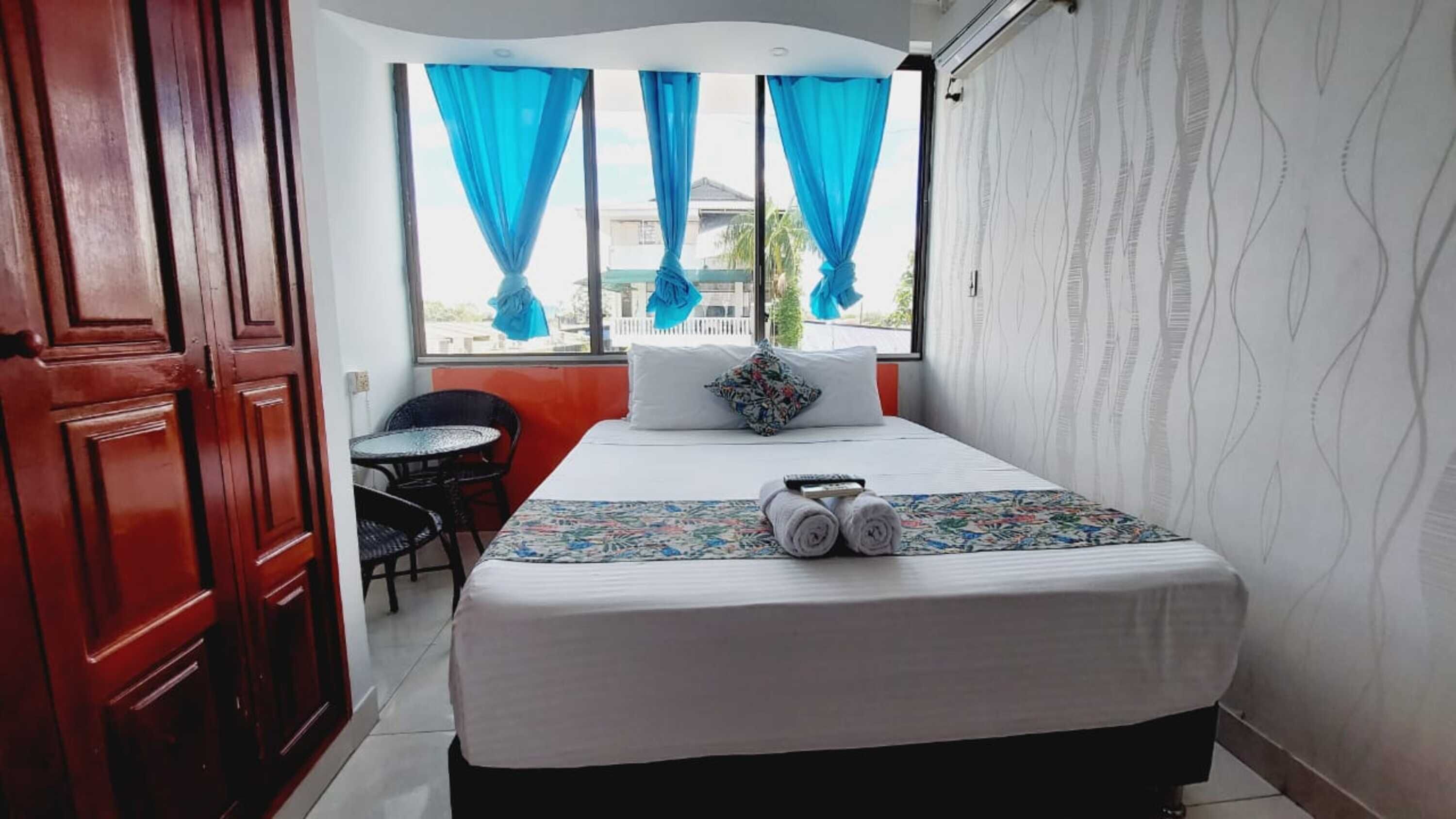 A hotel room with a bed, a small table, chairs, and a window with curtains.