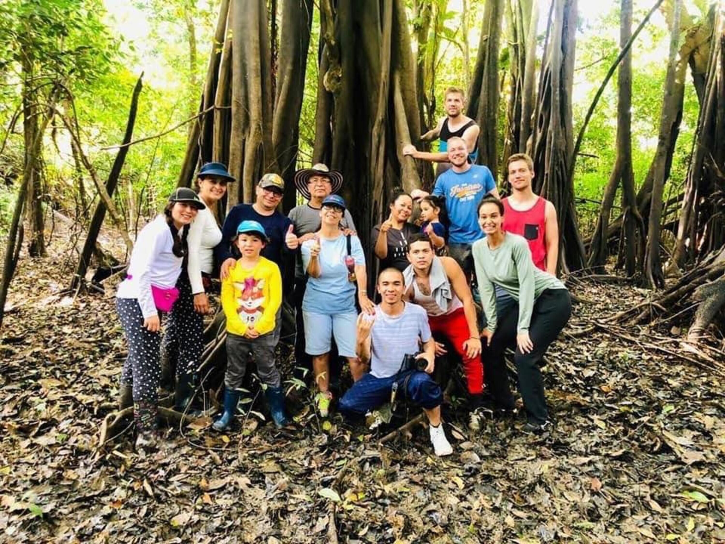 A group of people posing in a forested area with tall trees and leaf-covered ground.