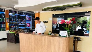 A reception desk with a wooden finish, a potted plant with red flowers, and a wall-mounted sign. - Hotel Yurupary (Leticia)