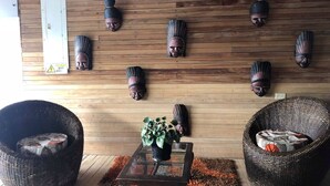 A room with wooden panel walls, a glass-top table with a potted plant, two wicker chairs, and several wooden masks on the wall. - Hotel Yurupary (Leticia)