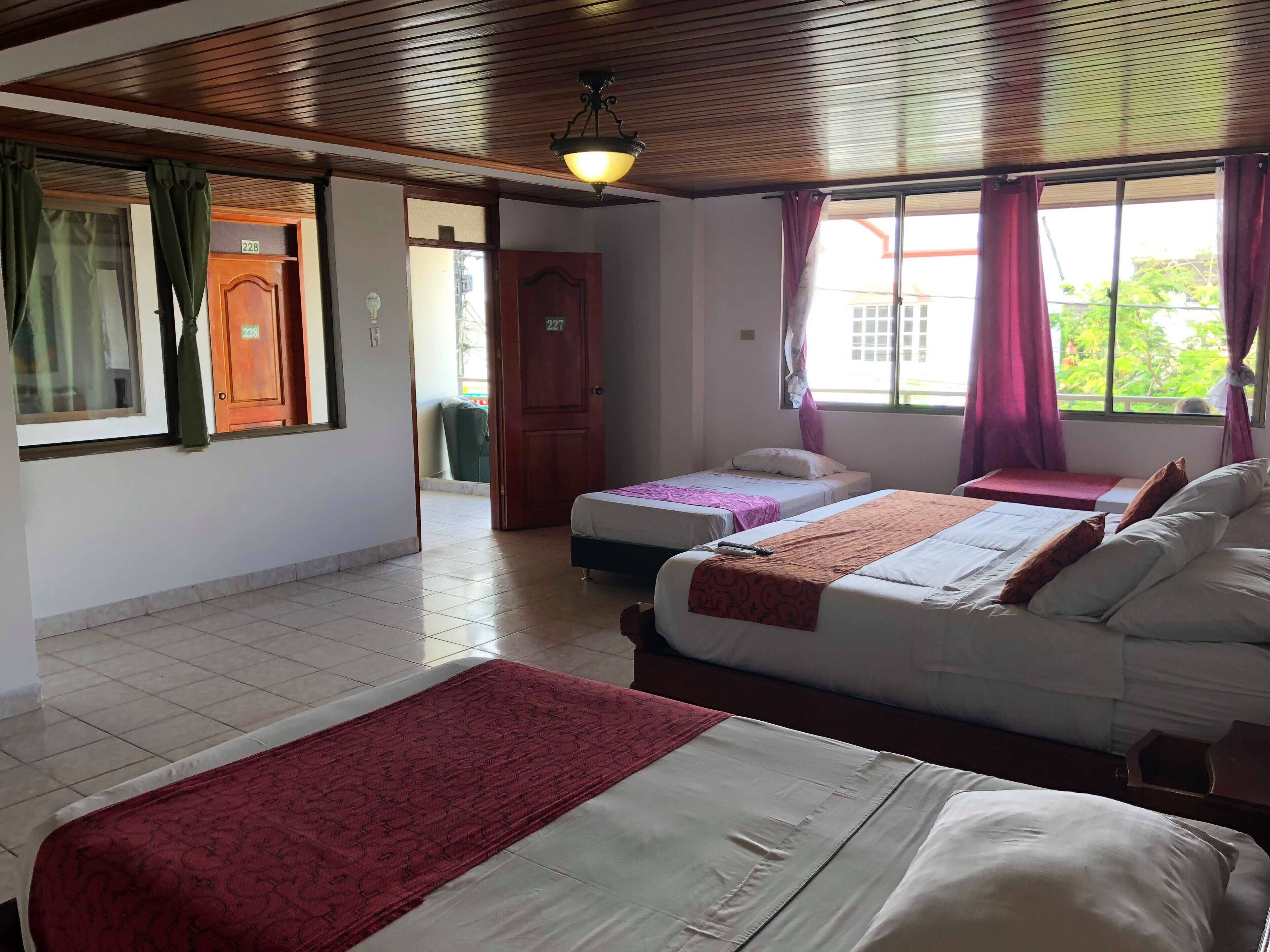 A hotel room with two beds, a wooden ceiling, and a view of the outside.