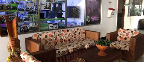 A room with a wicker sofa set, a potted plant, and a glass display case filled with electronic devices.