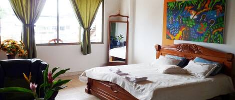 Een hotelkamer met een houten bed, een spiegel, een kleurrijk abstract schilderij en uitzicht op de stad.