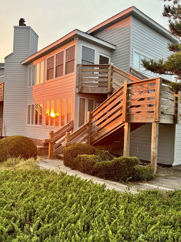 A two-story house with a wooden staircase leading to a deck.