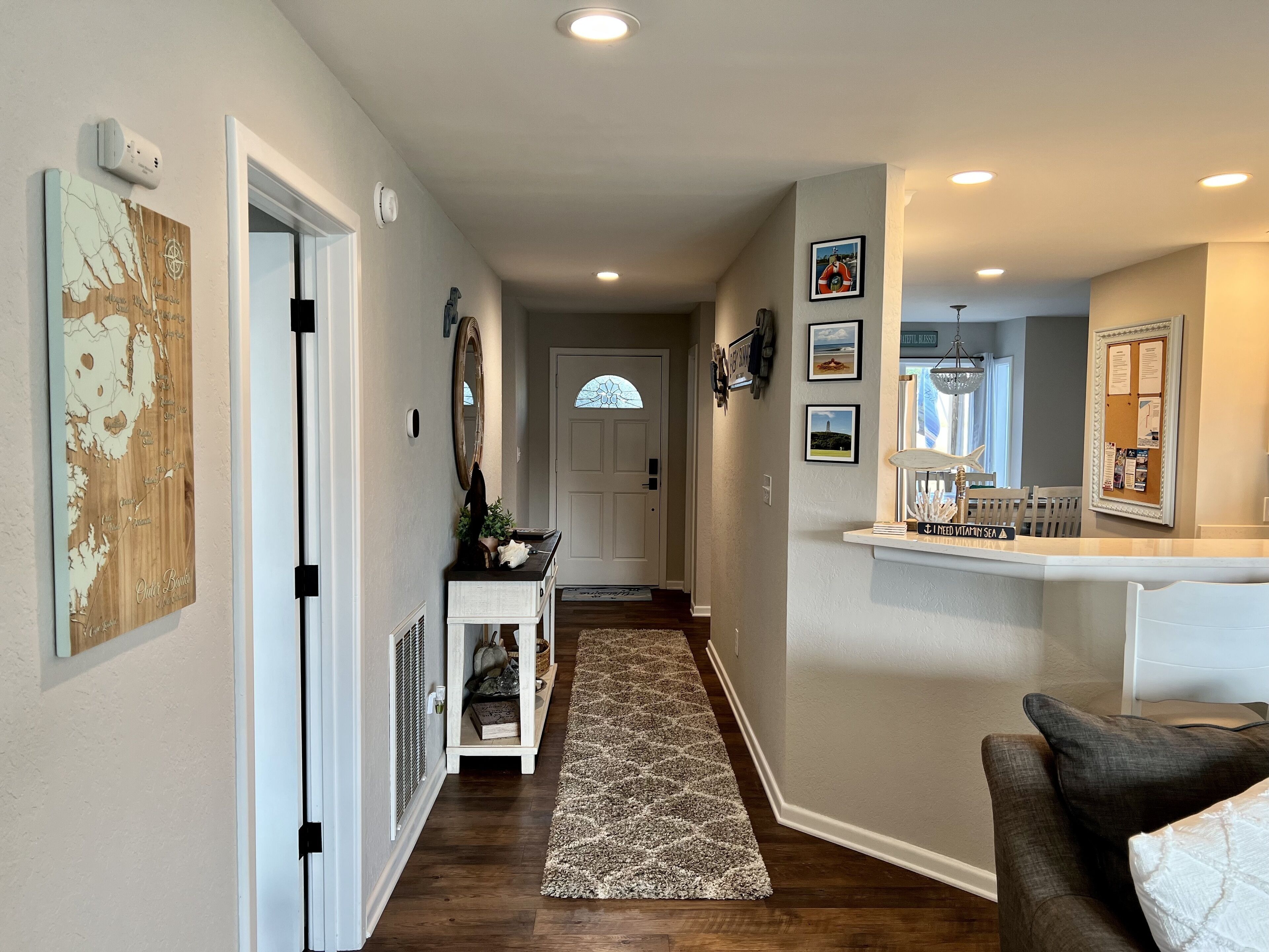 A hallway with a wooden floor, a white console table with decorative items, a rug, and a door leading to a room.