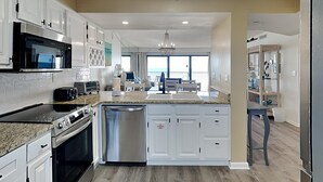 A modern kitchen with white cabinetry, stainless steel appliances, and a large island with a sink. - Emerald Towers by Southern Vacation Rentals (Destin)