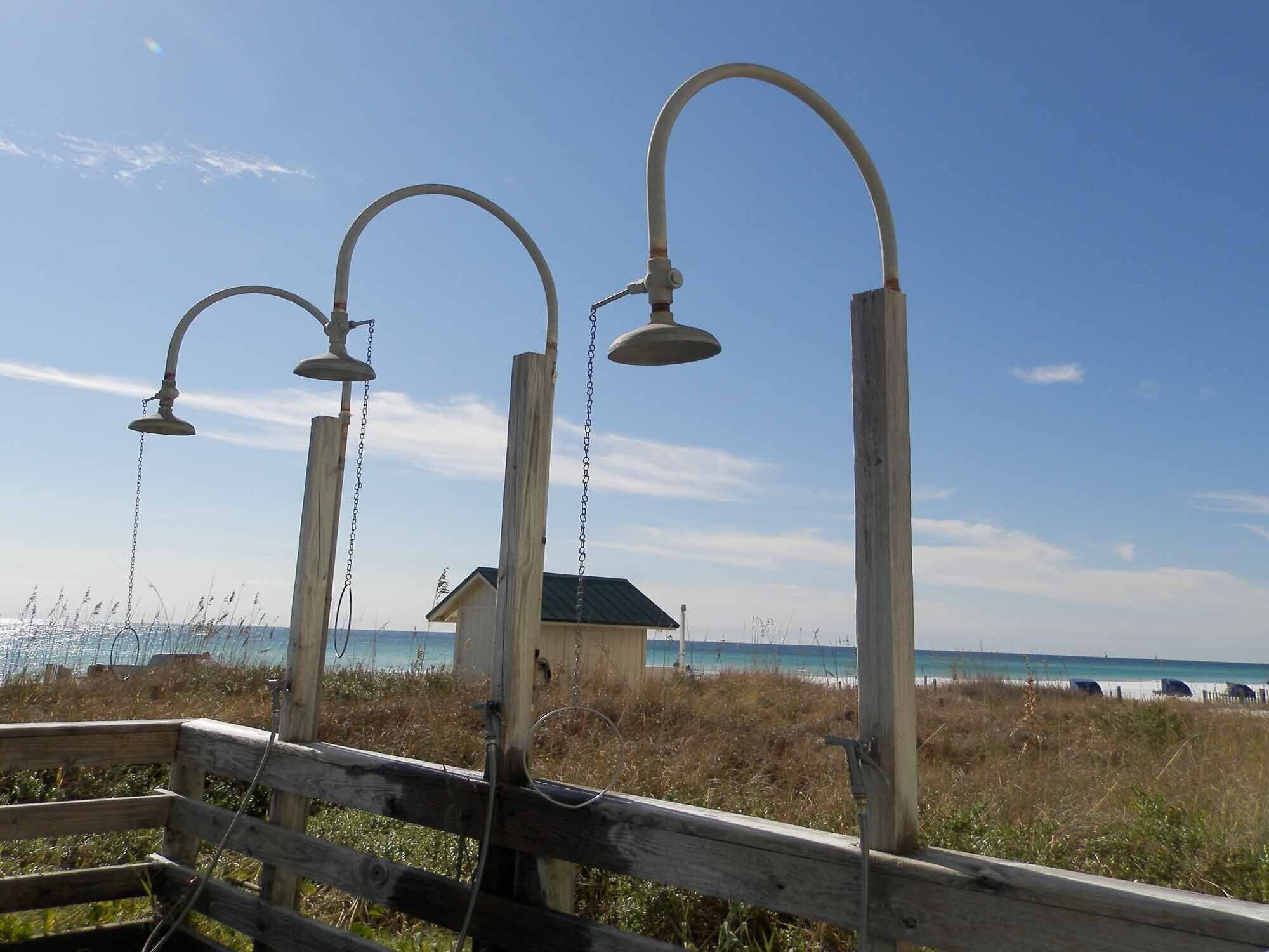 Una valla de madera con tres estructuras metálicas, posiblemente para agua o sonido, que da a una playa con cielo despejado.