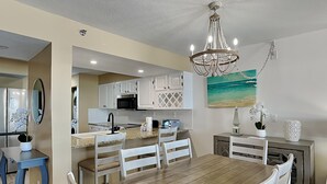 A modern kitchen with white cabinets, a wooden dining table, and a chandelier. - Emerald Towers by Southern Vacation Rentals (Destin)