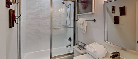 A modern bathroom with a glass-enclosed shower, a white toilet, and a sink with a mirror.