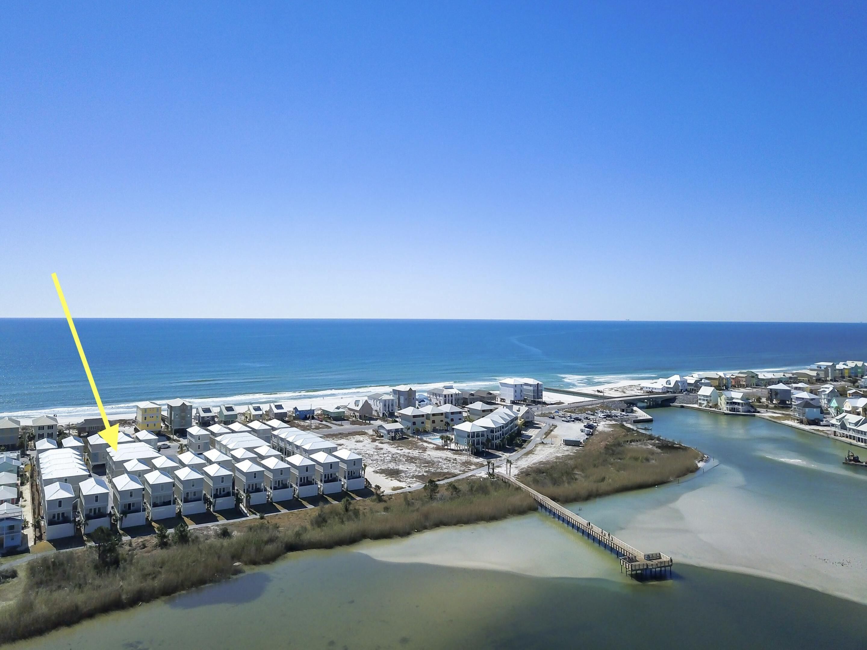 An aerial view of a coastal residential area with multiple white houses, a beach, and a waterway.