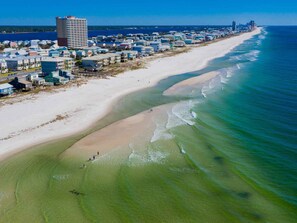 A coastal town with a long sandy beach, clear blue waters, and a mix of residential and commercial buildings.