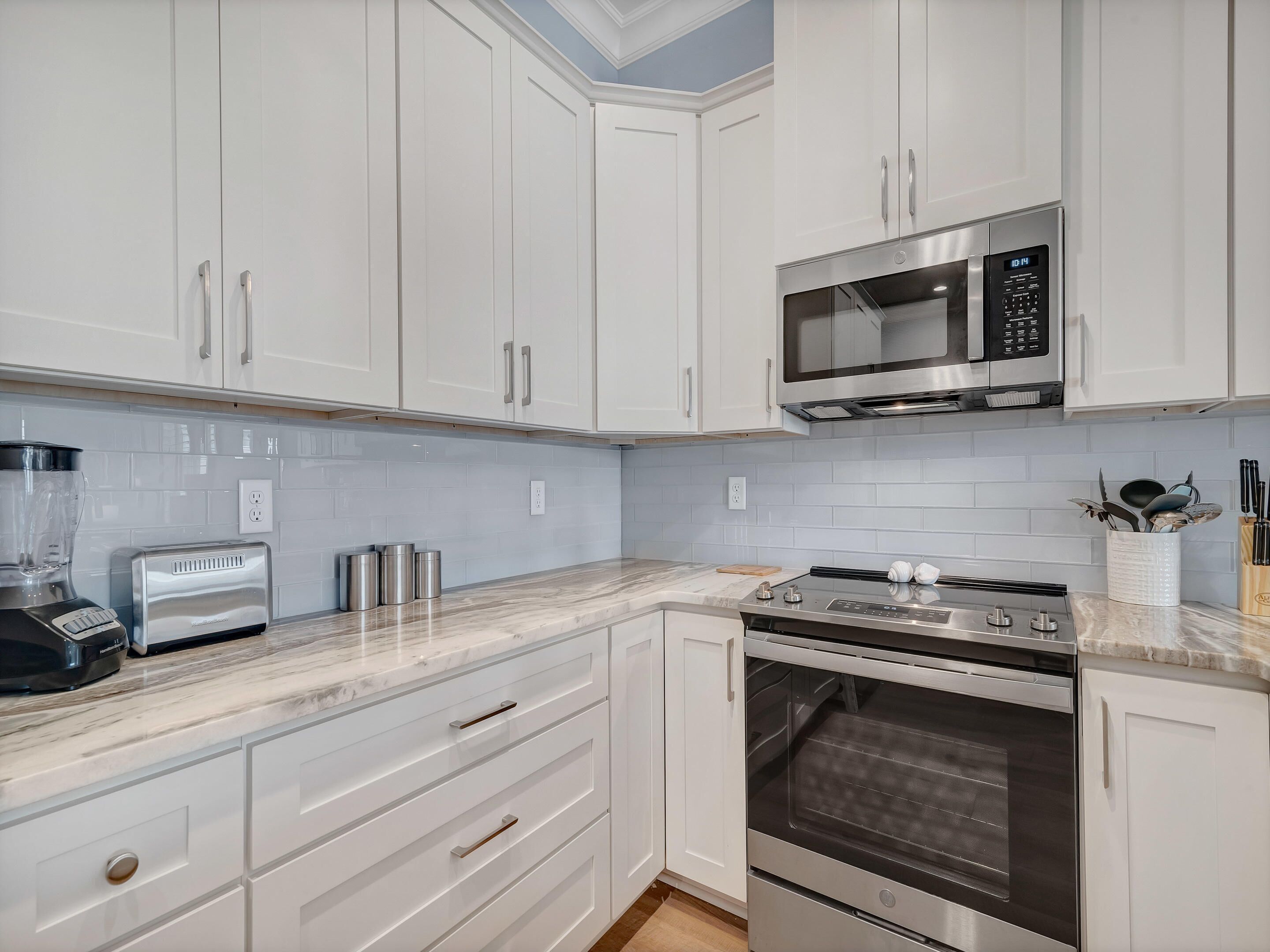A modern kitchen with white cabinets, a built-in microwave, a toaster, and an oven.
