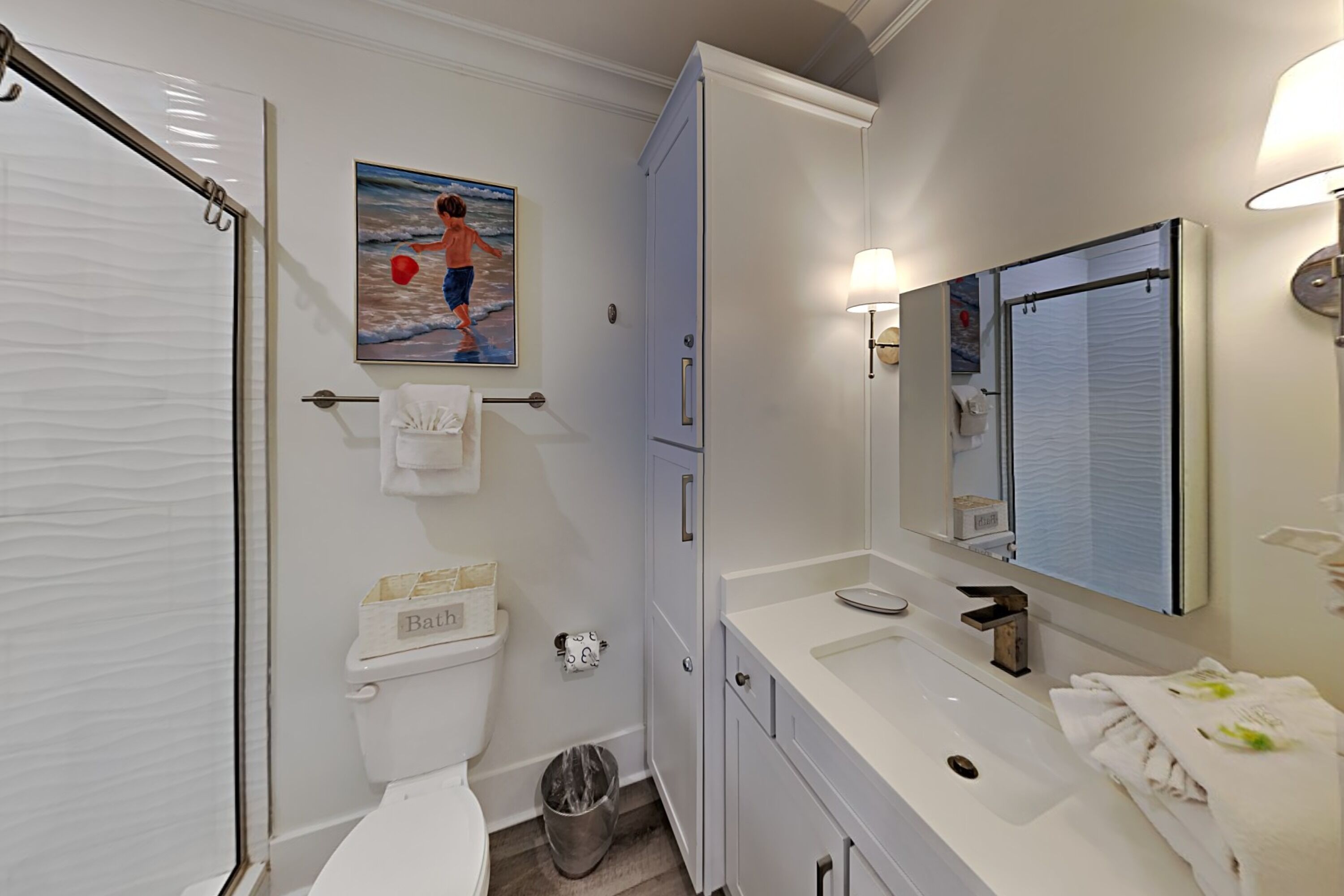 Ein Badezimmer mit Toilette, Waschbecken, Spiegel und einem Bild von einem Kind, das im Meer spielt.