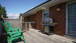 Un patio con una parrilla, una silla verde y un muro de ladrillo.