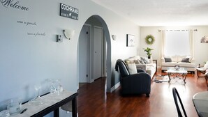 Una sala de estar moderna con un sofá, sillones y una mesa de centro. Hay un letrero en la pared que dice "Welcome" y "COCHRANE 49.06 N 01.02 W".
