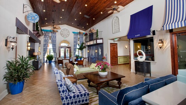 A spacious lobby with a high ceiling, wooden beams, and ceiling fans. There are multiple seating areas with patterned sofas and a dining table. - Stylish 4BR Townhome, Themed Rooms, Private Pool. Near Disney! (Kissimmee)
