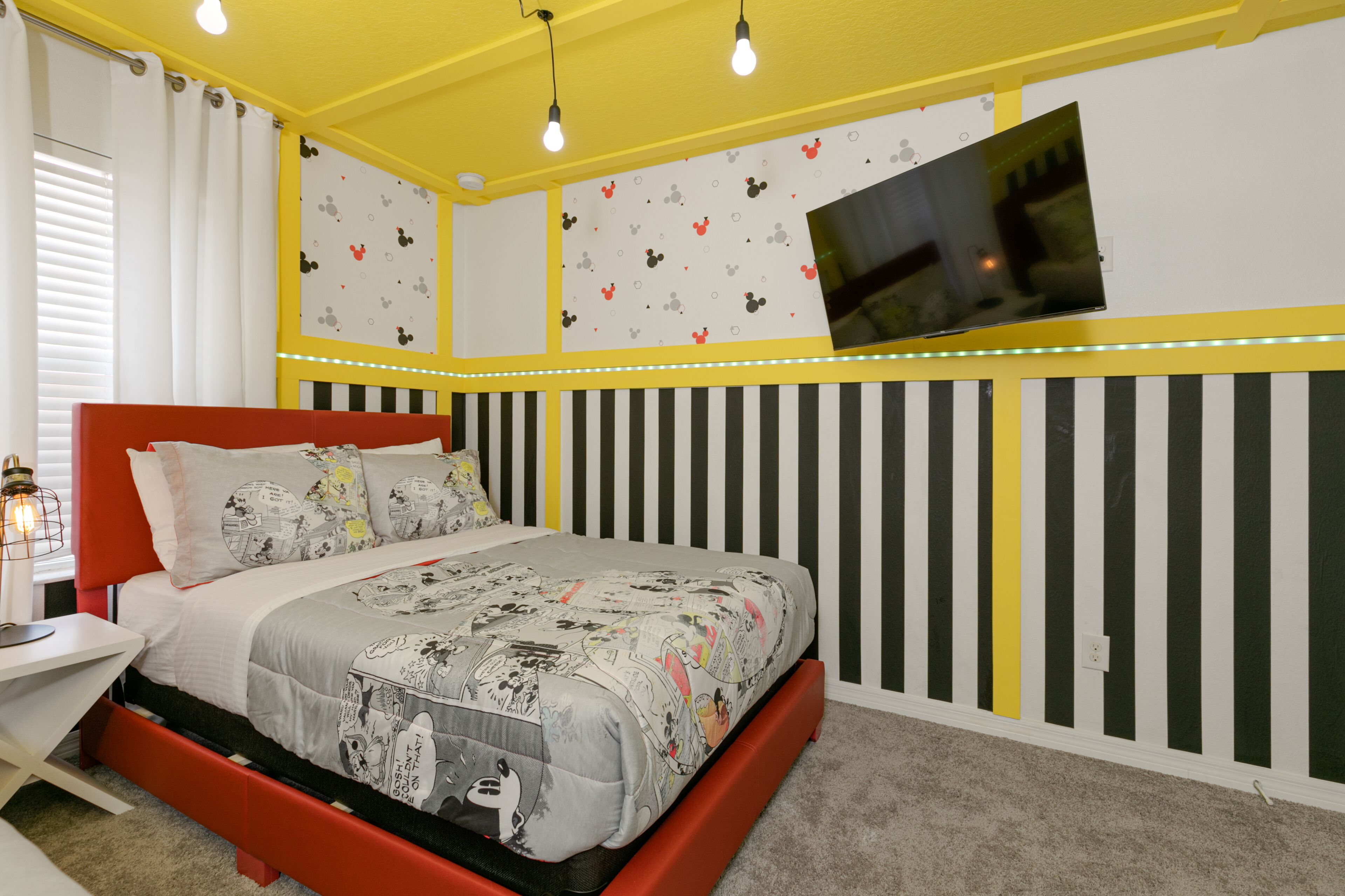 Een slaapkamer met een bed, een nachtkastje, een aan de muur bevestigde televisie en een raam met gordijnen.