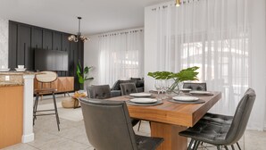 A modern dining area with a wooden table, black chairs, and a TV mounted on the wall. - Stylish 4BR Townhome, Themed Rooms, Private Pool. Near Disney! (Kissimmee)