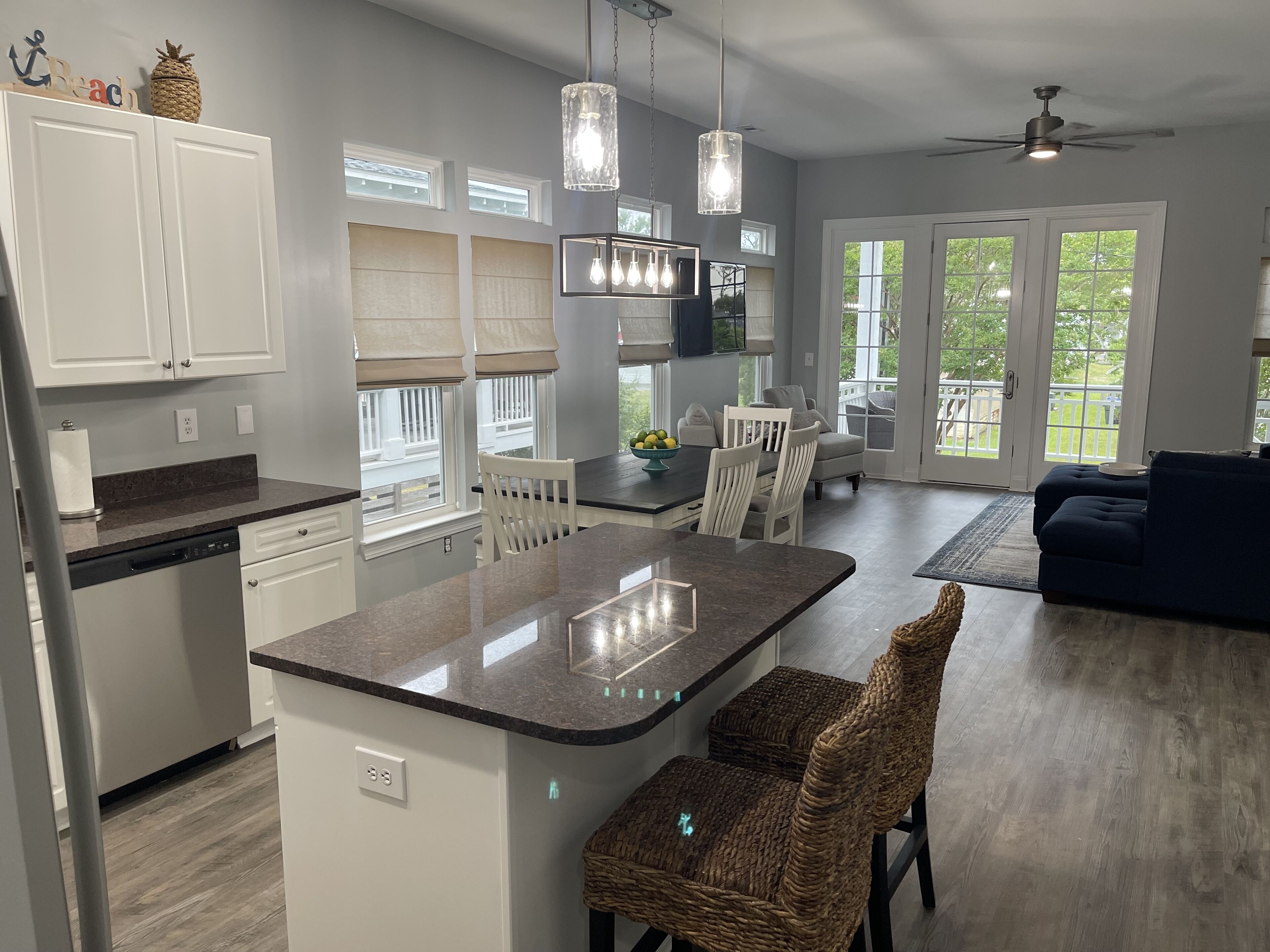 A modern kitchen with white cabinets, a central island, and a dining area with a dark blue sofa and wicker chairs.