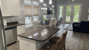 Cocina moderna con armarios blancos, una isla central y un comedor con sofá azul oscuro y sillas de mimbre.