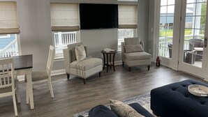 Una sala de estar con un sofá gris, dos sillones, una mesa de comedor con sillas y un televisor montado en la pared.