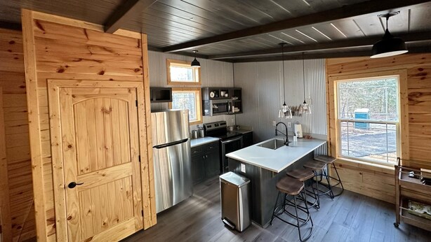 Een moderne keuken met houten wanden, een roestvrijstalen koelkast, een spoelbak en barstoelen.